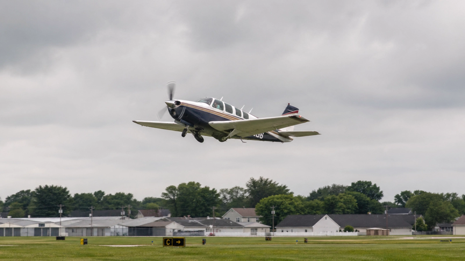 Beechcraft Bonanza aircraft climbing after takeoff from a suburban airport